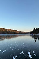 Eine große gefrorene Fläche, auf der Menschen Schlittschuh laufen und Bäume das Eis umgeben.