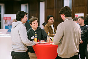 Conference participants stand together at a bar table and chat.