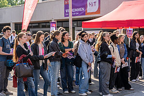 Eine Gruppe Menschen steht vor einem Pavillon mit einem roten Dach. Alle halten Broschüren in der Hand