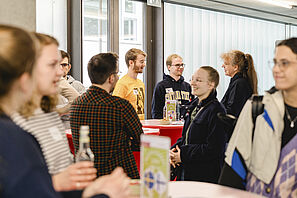 Studierende und Beratende unterhalten sich während der Outgoing-Messe an Stehtischen miteinander.