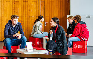 Studierende sitzen mit Studieninteressierten auf Sitzwürfeln und unterhalten sich