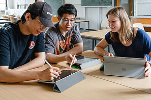 Drei Studierende sitzen an einem Tisch und lernen gemeinsam.
