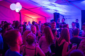 Einige Menschen tanzen in einem bunt beleuchteten Zelt.