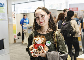 A student holds up a small TU fabric lion to the camera.