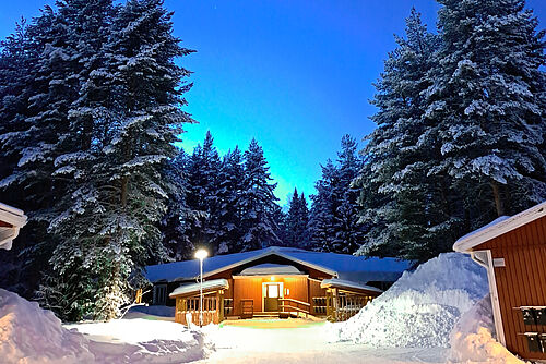 Eine beleuchtete Hütte in einem verschneiten Wald in Schweden.