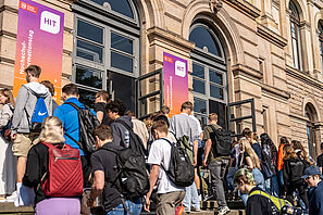 Eine Gruppe Menschen steigt die Treppe zum Altgebäude der TU Braunschweig hinauf. An der Fassade hängen zwei Banner auf denen das HIT Logo zu sehen ist.