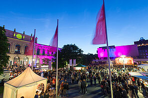 Zelte, Wägen und viele Menschen auf dem bunt beleuchteten Universitätsplatz der TU Braunschweig