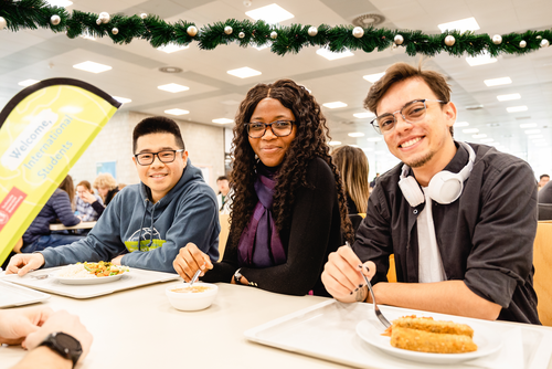 Drei internationale Studierende sitzen in der Mensa und nehmen an der International Lunch Break teil.