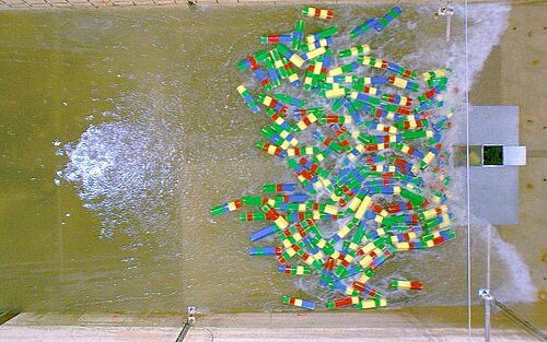 Ein Trümmer-Teppich in Treibgut in Form von farbigen Holzklötzen trifft auf die Säule im Wellenkanal.