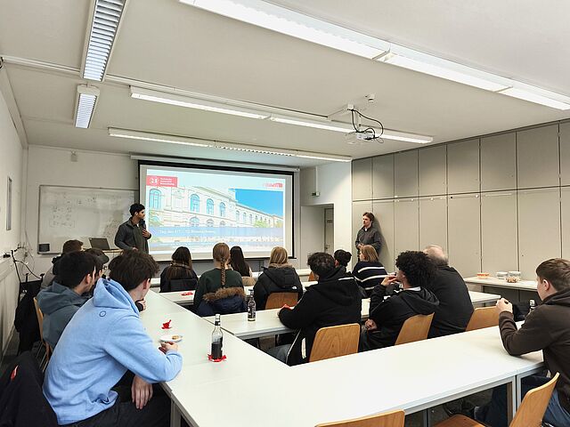 Schülerinnen und Schüler sitzen in einem Raum und ihnen werden Studiengänge vorgestellt