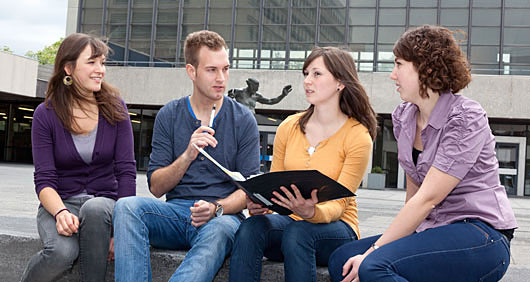 Vier Studierende sitzen vor dem Audimax und unterhalten sich angeregt.