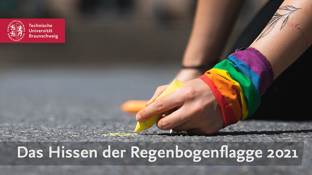 Eine mit der Regenbogenflagge umwickelte Hand malt mit gelber Kreide.